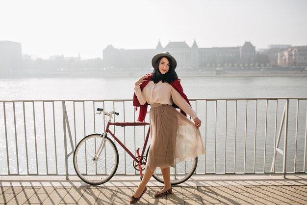 Grazioso modello femminile in posa con le gambe incrociate sulla parete del fiume