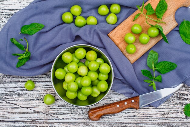 Greengages con foglie in una casseruola di metallo e tagliere di legno con coltello piatto giaceva su legno grigio e panno da picnic