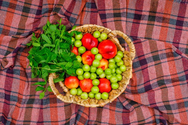 Greengages e pesche con le foglie in un canestro di vimini sul panno di picnic. vista dall'alto.