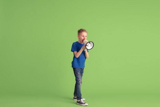 Gridare, chiamare. Ragazzo felice che gioca e si diverte sulla parete verde. Il bambino caucasico in un panno luminoso sembra giocoso, sorridente. Concetto di educazione, infanzia, emozioni, espressione facciale.