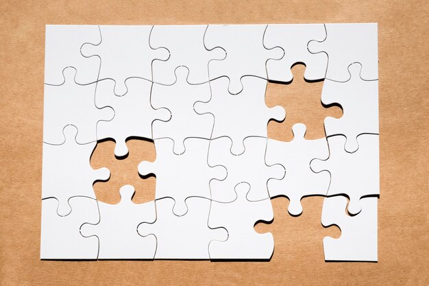 Griglia bianca di puzzle con il pezzo mancante di puzzle su carta marrone strutturata
