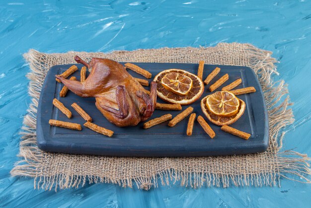 Griglia, limone essiccato e crostini su un vassoio sul tovagliolo di juta, sulla superficie blu.