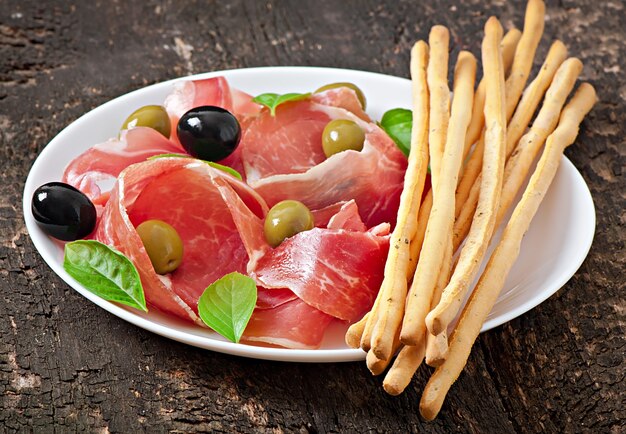 Grissini con prosciutto, olive, basilico su legno vecchio