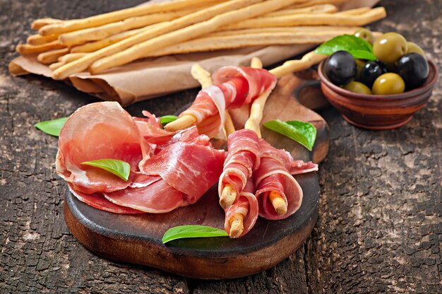 Grissini con prosciutto, olive, basilico su legno vecchio