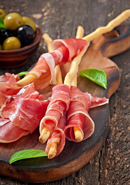 Grissini con prosciutto, olive, basilico su legno vecchio