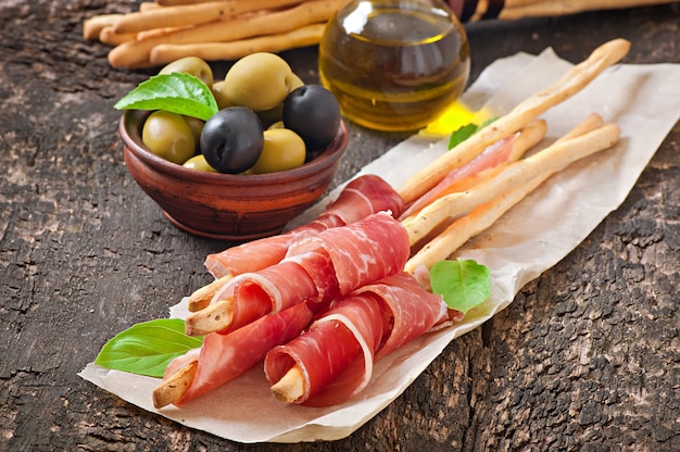 Grissini con prosciutto, olive, basilico su legno vecchio