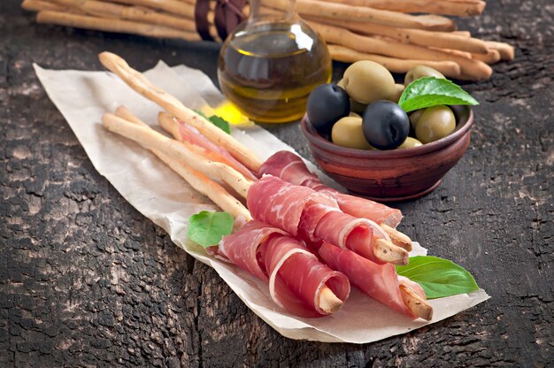 Grissini con prosciutto, olive, basilico su legno vecchio