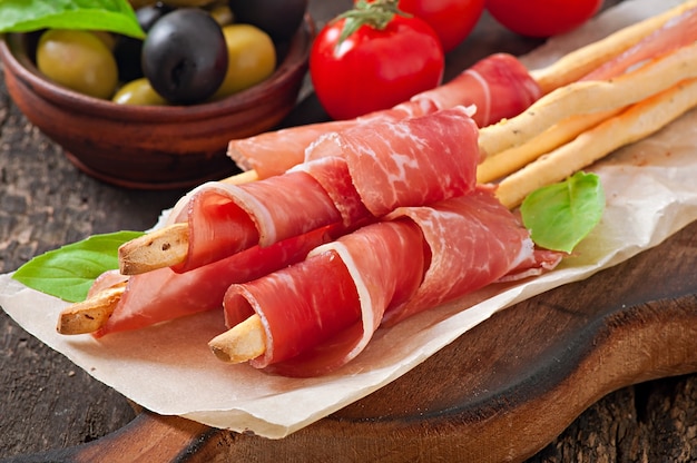 Grissini con prosciutto, olive, basilico su legno vecchio