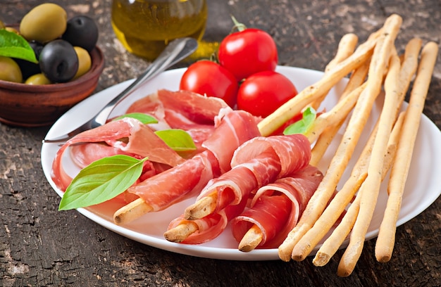 Grissini con prosciutto, olive, basilico su legno vecchio