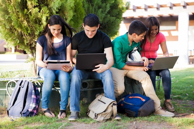 Gruppo di adolescenti che fanno social networking utilizzando diversi dispositivi tecnologici al liceo