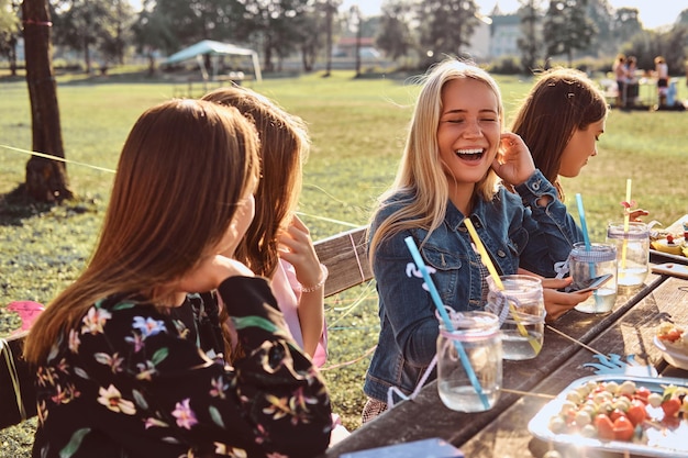 Gruppo di amiche sedute al tavolo insieme per festeggiare un compleanno nel parco all'aperto.