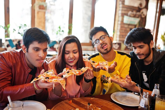 Gruppo di amici asiatici che mangiano pizza durante la festa in pizzeria Gli indiani felici si divertono insieme a mangiare cibo italiano e seduti sul divano