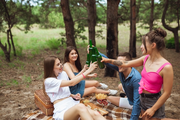 Gruppo di amici che clinking le bottiglie di birra durante il picnic nella foresta di estate