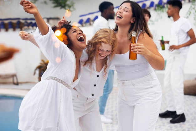 Gruppo di amici che si divertono durante una festa bianca con drink a bordo piscina