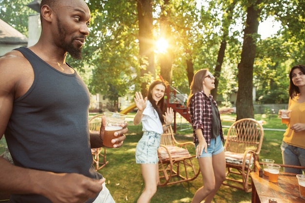 Gruppo di amici felici che hanno birra e barbecue party in giornata di sole. Riposare insieme all'aperto in una radura della foresta o in un cortile