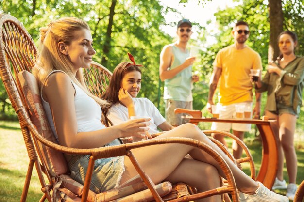 Gruppo di amici felici che hanno birra e barbecue party in giornata di sole. Riposare insieme all'aperto in una radura della foresta o in un cortile