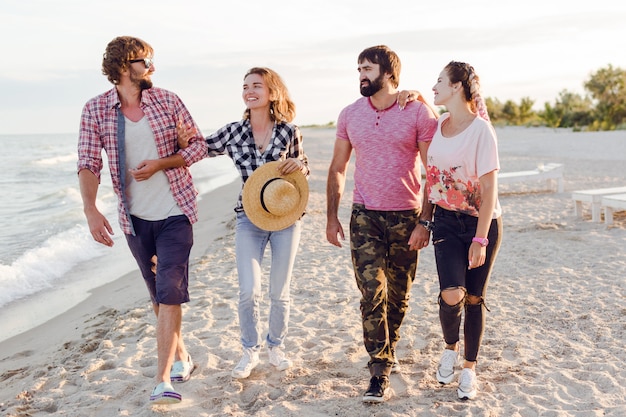 Gruppo di amici felici che trascorrono del tempo insieme e camminano lungo la spiaggia assolata