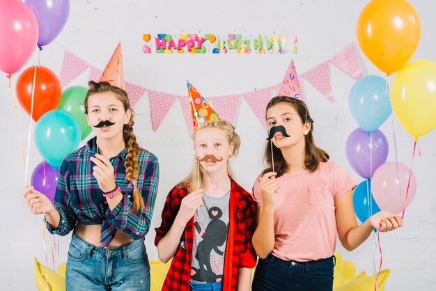 Gruppo di amici in posa con i baffi di puntello durante il compleanno