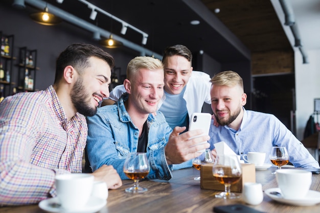 Gruppo di amici maschi guardando smartphone seduto al ristorante con bevande sul tavolo