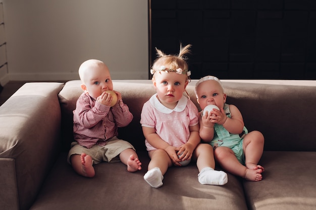 Gruppo di bambini carini divertenti seduti insieme sul divano a giocare con palline colorate. Tre ragazzini felici e ragazze in abiti colorati in posa su un comodo divano a tutto campo