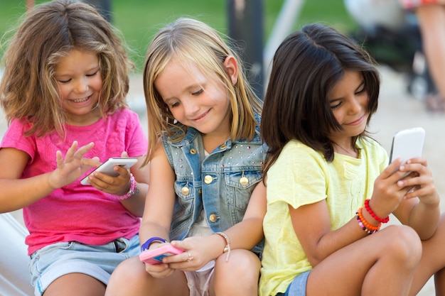 Gruppo di bambini che chiacchierano con i telefoni astuti nel parco.