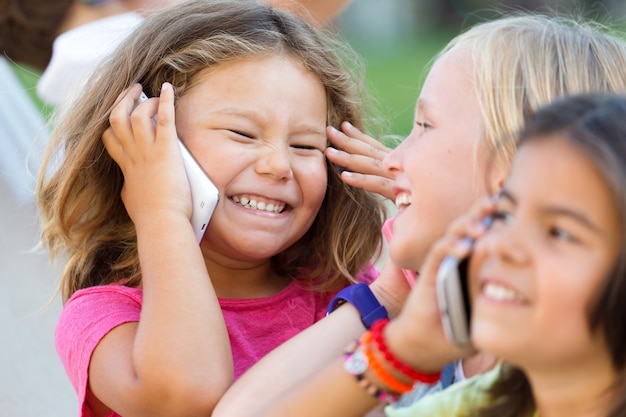 Gruppo di bambini che usano i telefoni mobili nel parco.