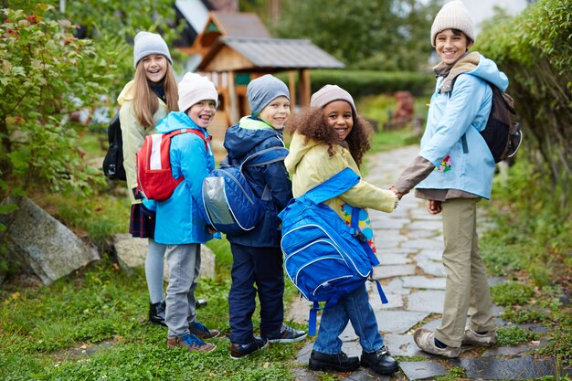 Gruppo di bambini felici che camminano a scuola in autunno