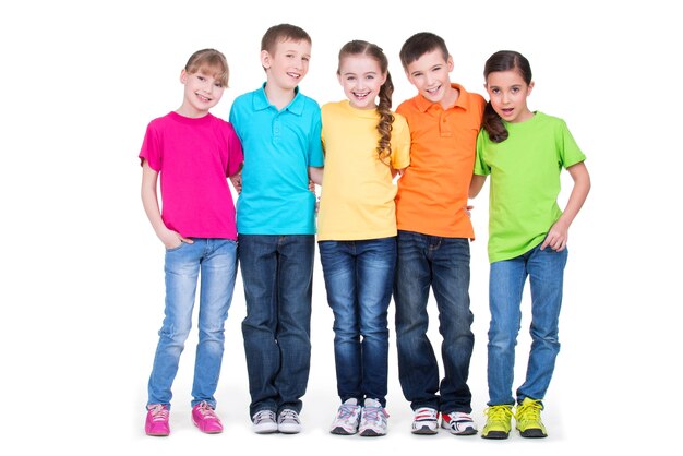 Gruppo di bambini felici in magliette colorate che stanno insieme in piena lunghezza su sfondo bianco.