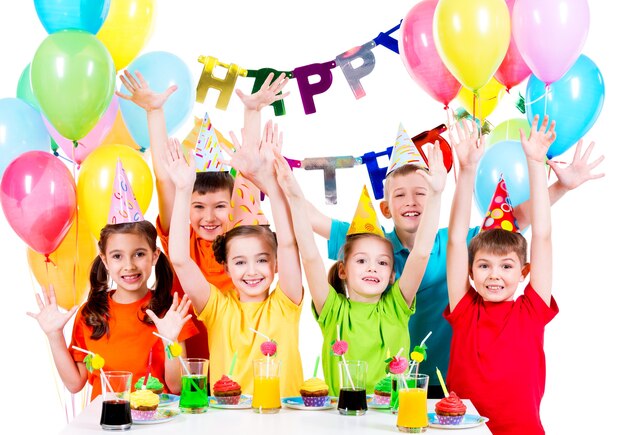 Gruppo di bambini in camicie colorate alla festa di compleanno con le mani alzate - isolato su un bianco