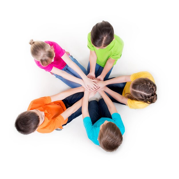 Gruppo di bambini sorridenti che si siedono sul pavimento in un cerchio che tengono le mani - isolato su bianco.