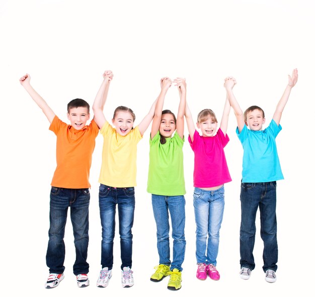 Gruppo di bambini sorridenti con le mani alzate in magliette colorate che stanno insieme - isolato su bianco.