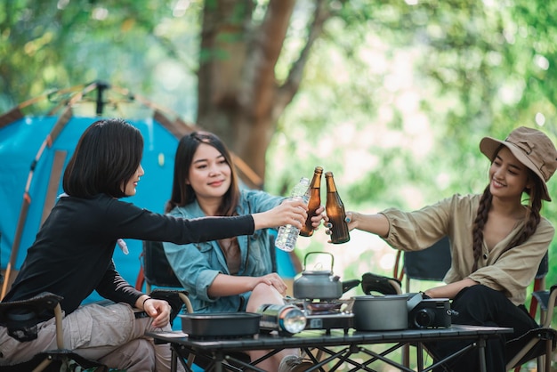 Gruppo di belle donne asiatiche amici viaggiatori che si rilassano davanti alla tenda da campeggio Si divertono a parlare e bere birra divertendosi e felici insieme