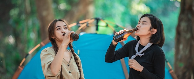 Gruppo di belle donne asiatiche amici viaggiatori che si rilassano davanti alla tenda da campeggio Si divertono a parlare e bere birra divertendosi e felici insieme