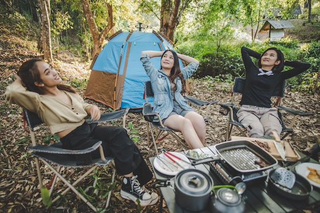 Gruppo di belle donne sedute su una sedia da campeggio davanti alla tenda per rilassarsi mentre si accampa nella foresta naturale con felicità insieme copia spazio