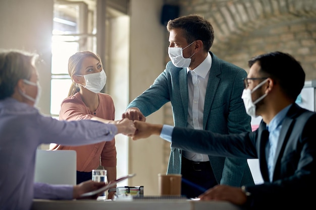 Gruppo di colleghi che indossano maschere protettive e urtano i pugni durante una riunione di lavoro durante la pandemia di coronavirus