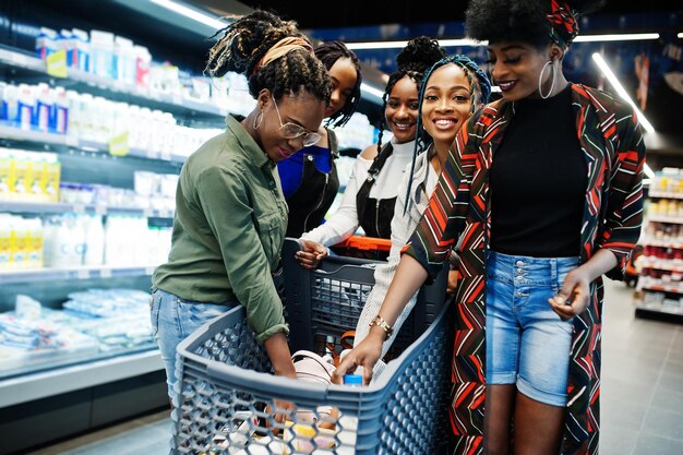 Gruppo di donne africane con carrelli della spesa vicino allo scaffale del frigorifero che vendono prodotti lattiero-caseari a base di latte al supermercato