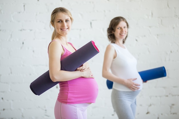 Gruppo di donne in gravidanza di forma fisica che tengono gli sport tappeti