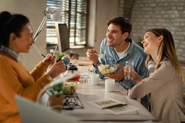 Gruppo di felici lavoratori freelance che parlano e si divertono durante la pausa pranzo in ufficio