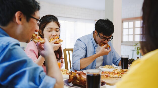 Gruppo di giovani amici felici a pranzo a casa. Festa della famiglia asiatica che mangia pizza e che ride gustando un pasto seduti al tavolo da pranzo insieme a casa. Celebrazione vacanza e stare insieme.