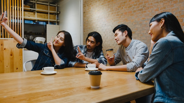 Gruppo di giovani asiatici felici che si divertono e fanno selfie con la sua amica seduti insieme al bar ristorante.