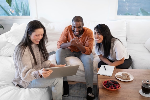 Gruppo di giovani che usano il laptop insieme a casa sul divano e mangiano spuntini