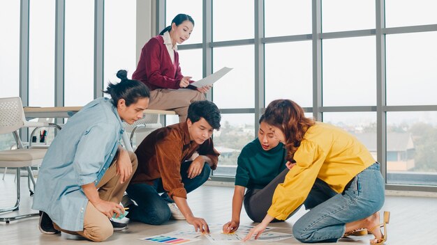 Gruppo di giovani creativi asiatici in abbigliamento casual discutendo di idee riunione di brainstorming di affari piano di progetto di progettazione di software applicativo mobile disposto sul pavimento in ufficio. Concetto di lavoro di squadra del collega.