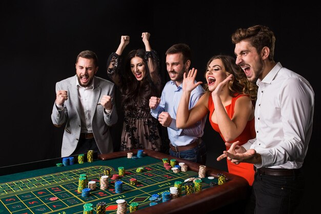 Gruppo di giovani dietro il tavolo della roulette su sfondo nero. I giovani hanno fatto scommesse nel gioco e aspettano il risultato. Emozioni luminose