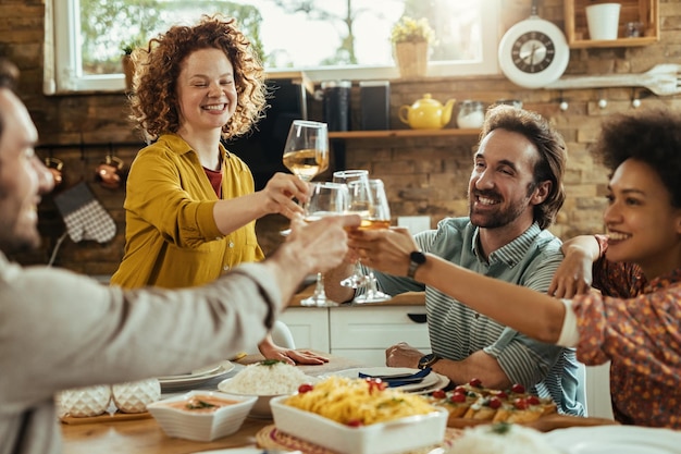 Gruppo di giovani felici divertendosi mentre brindano con il vino durante il pranzo al tavolo da pranzo