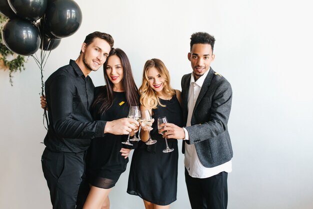Gruppo di giovani gioiosi in abiti alla moda alzando i bicchieri con champagne