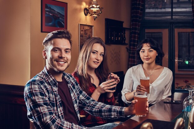 Gruppo di giovani sorridenti multirazziali che riposano nel pub. Amici seduti al bancone di legno e godendosi un drink.