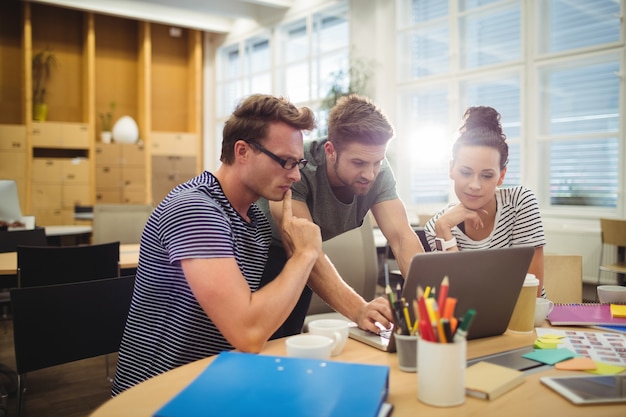 Gruppo di grafici che discute sopra computer portatile a loro scrivania