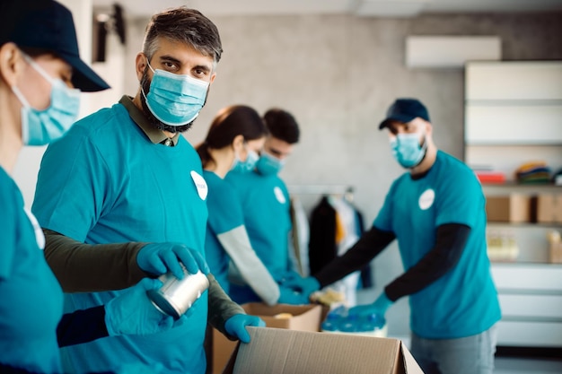 Gruppo di persone con maschere protettive che imballano scatole per donazioni per beneficenza alimentare