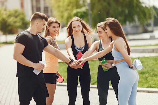 Gruppo di persone in un parco. Ragazzo con quattro ragazze. Sportivi con bottiglie d'acqua.