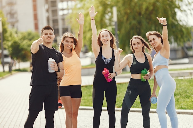 Gruppo di persone in un parco. Ragazzo con quattro ragazze. Sportivi con bottiglie d'acqua.